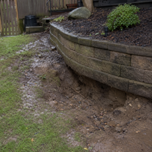 Soil erosion and exposed base near a masonry retaining wall.