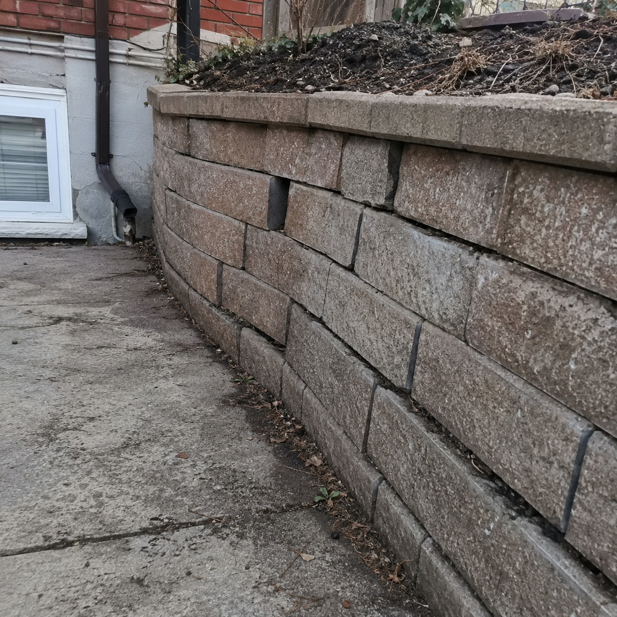 Bulging retaining wall with visible separation and movement in a residential yard.