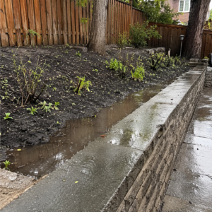 Water pooling behind a retaining wall after heavy rain.