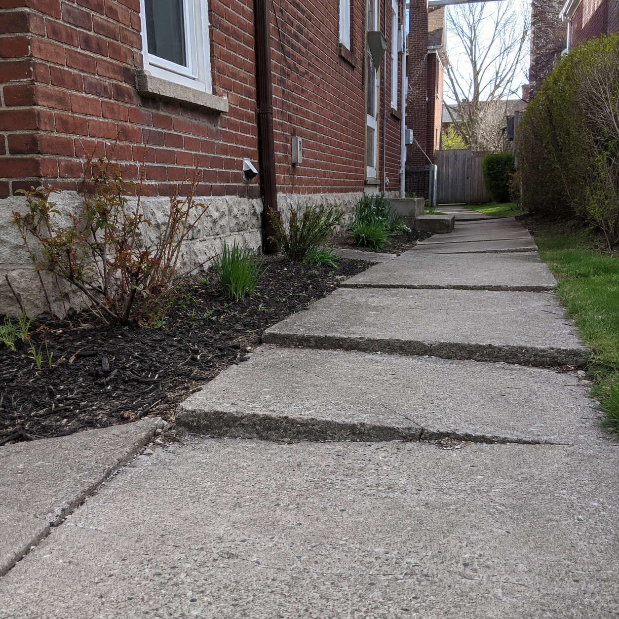 Uneven concrete walkway creating a trip hazard beside a brick home
