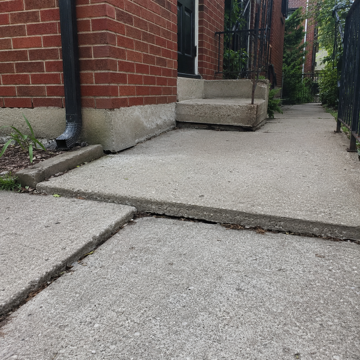 Sunken concrete slabs shifting near a residential brick foundation