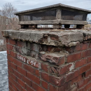 Spalling brick and failing mortar below a failed chimney cap.