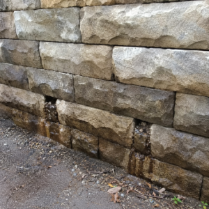 Blocked weep holes on a masonry retaining wall with damp staining.