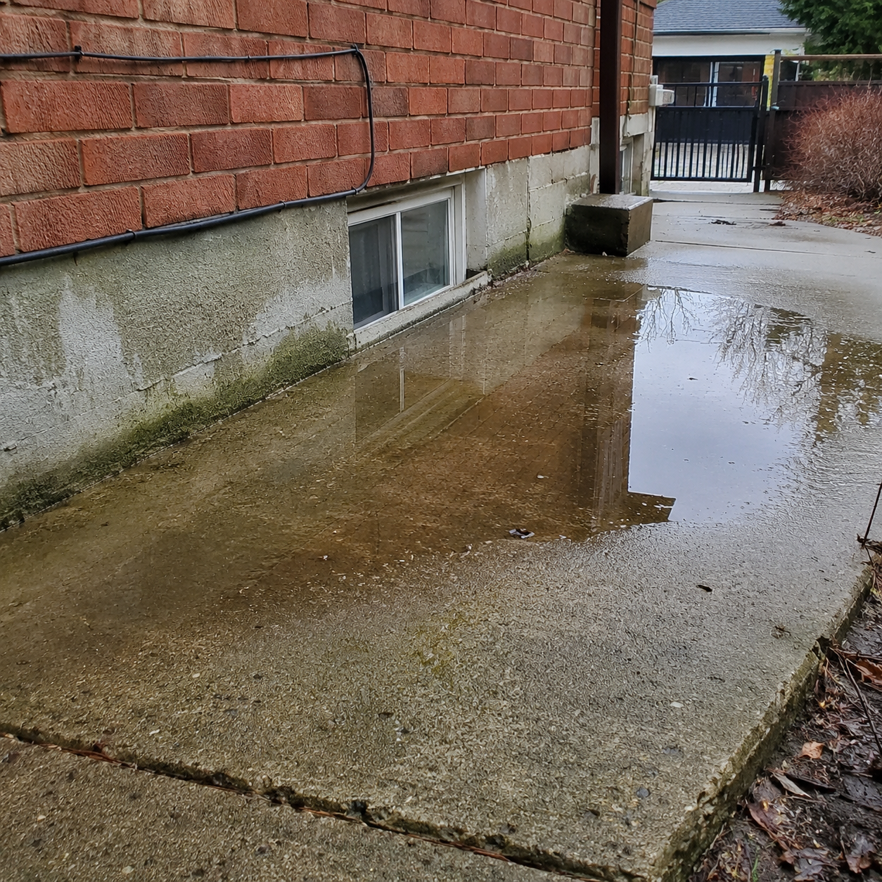 Water pooling near concrete surface beside a brick house