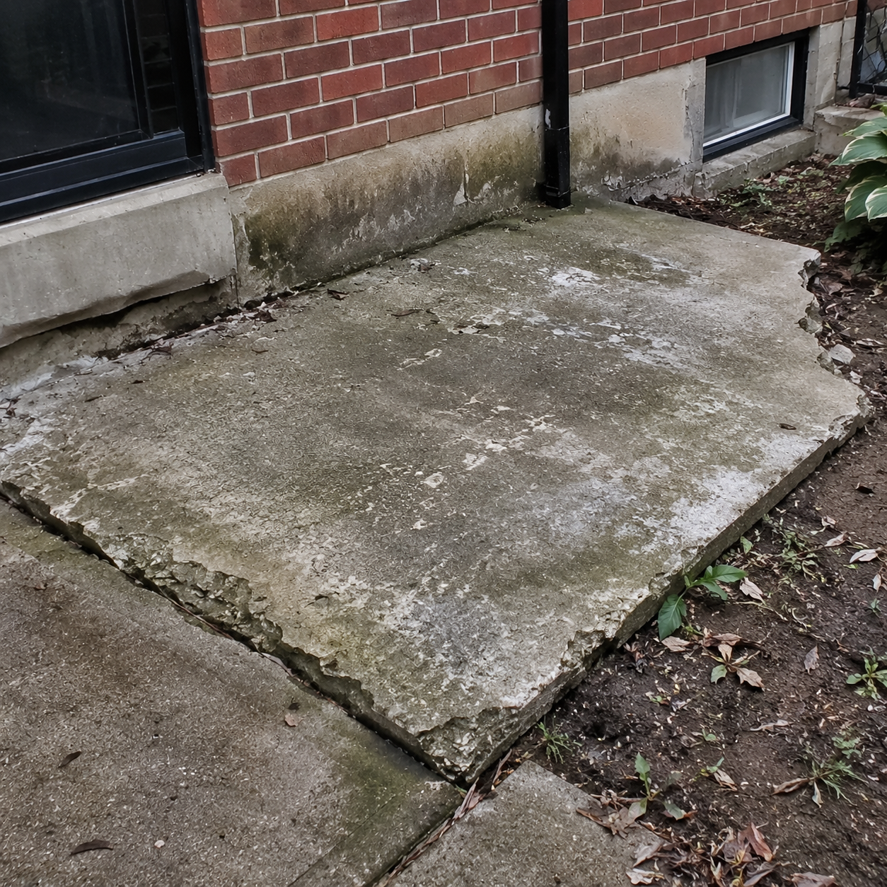 Deteriorated concrete pad beside an older brick home