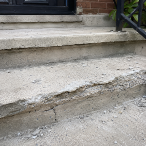 Close-up of cracked concrete steps with chipped edges and surface scaling.